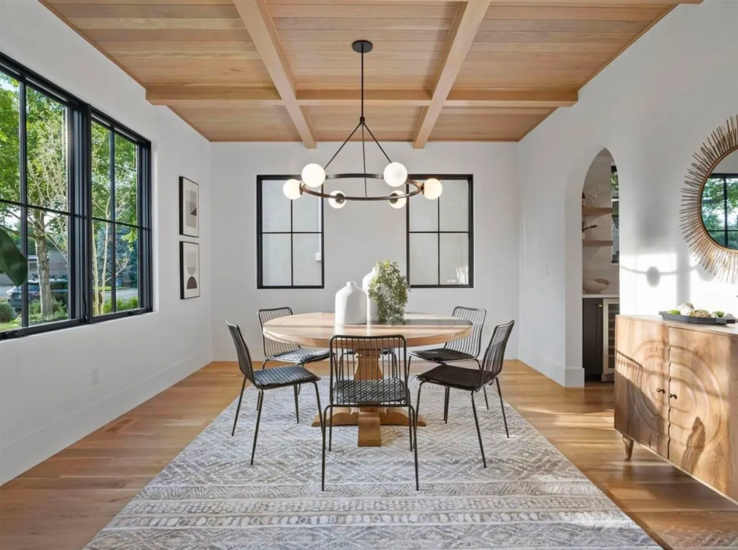 residential-interior-11 Modern dining room with a round table, black chairs, large windows, and contemporary chandelier.