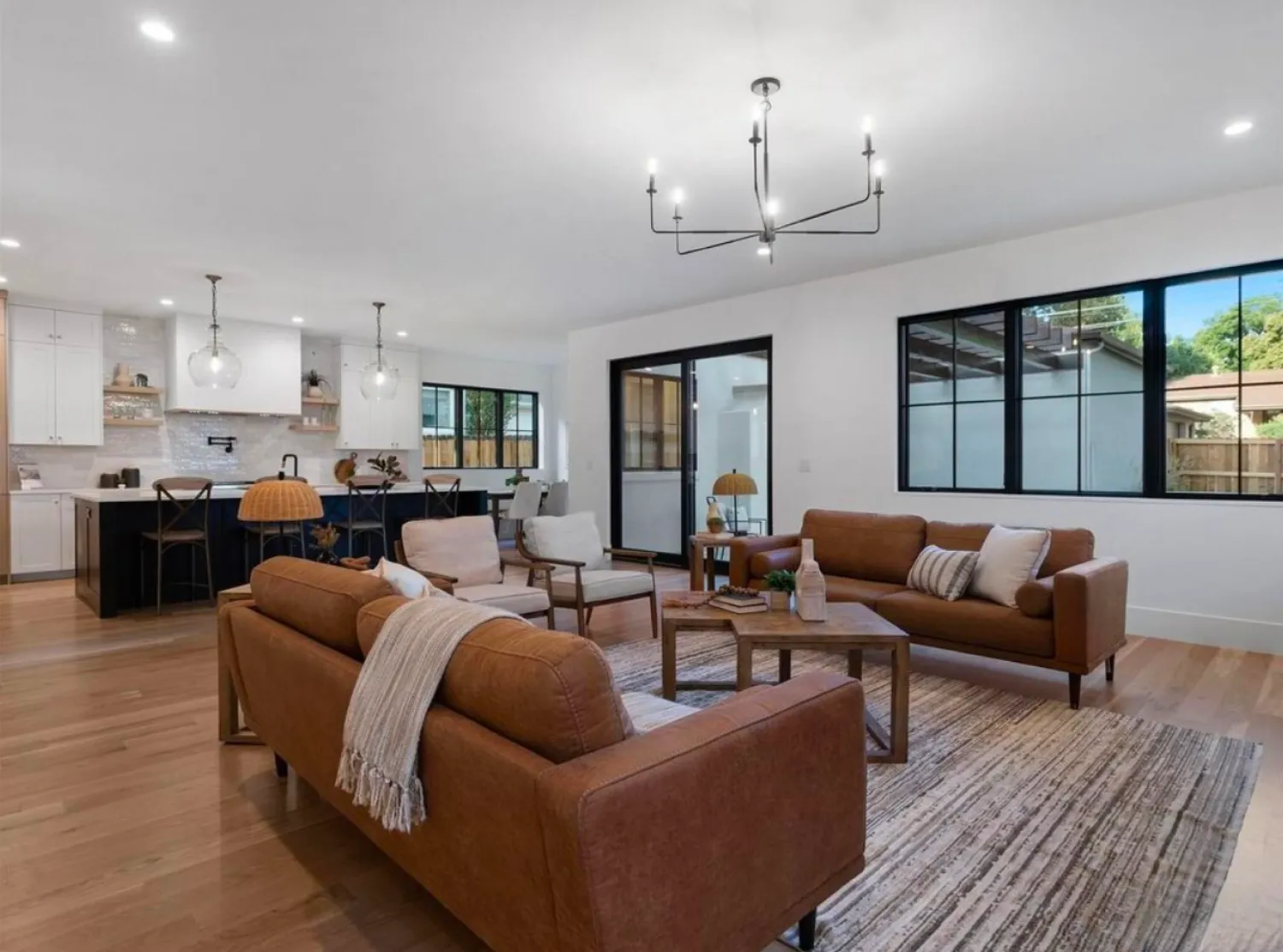 residential-interior-14 Modern open living room and kitchen with brown sofas, wooden accents, and large windows.