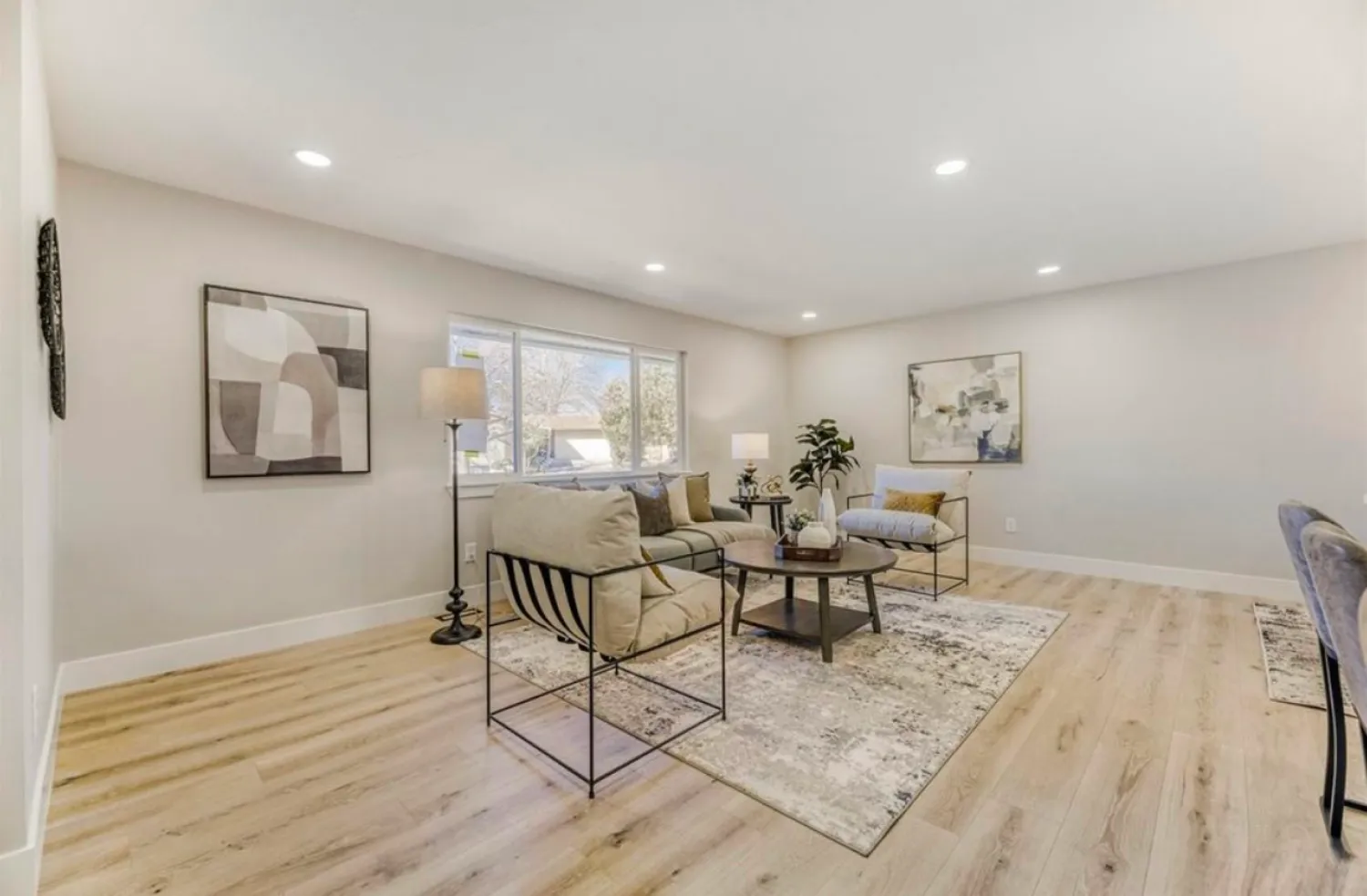 residential-interior-16 Modern living room with neutral decor, abstract art, light wood floors, and large window letting in sunlight.