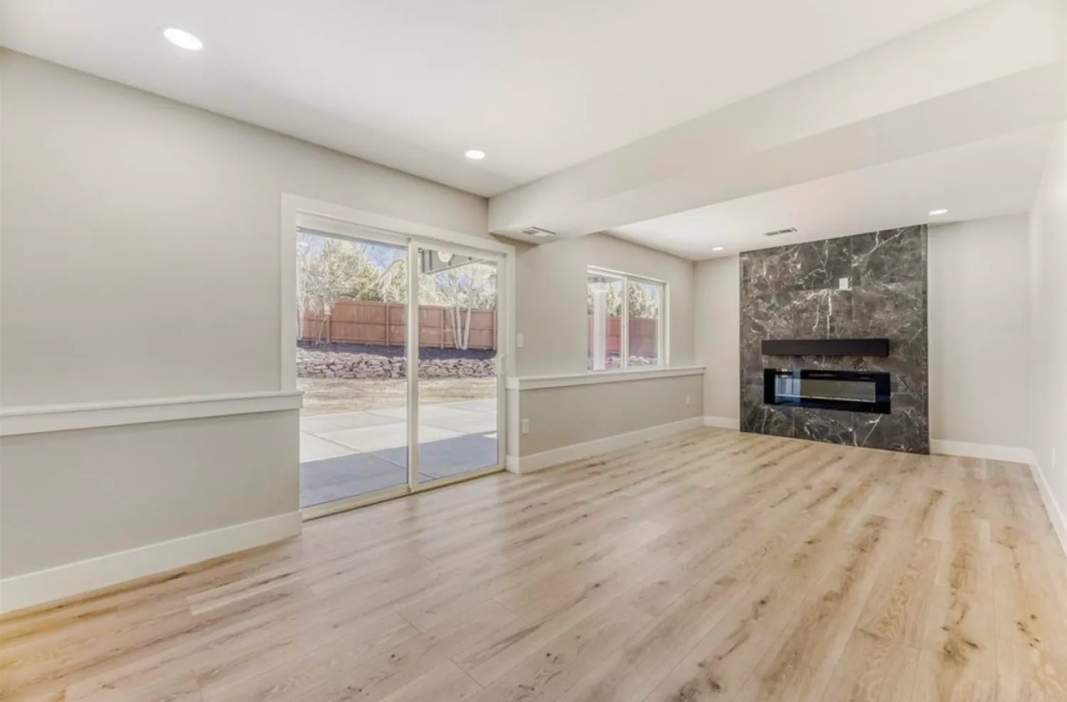 residential-interior-18 Bright living room with wood floor, sliding glass doors, and a modern black fireplace on a marble accent wall.