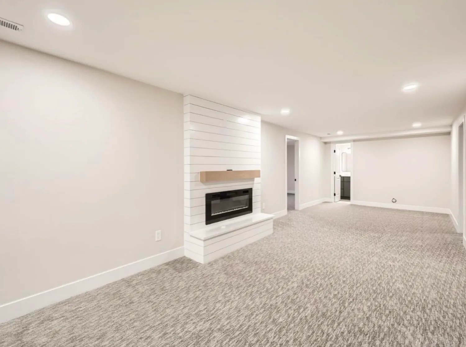 residential-interior-21 Modern finished basement with light walls, recessed lighting, and a fireplace on a shiplap accent wall.