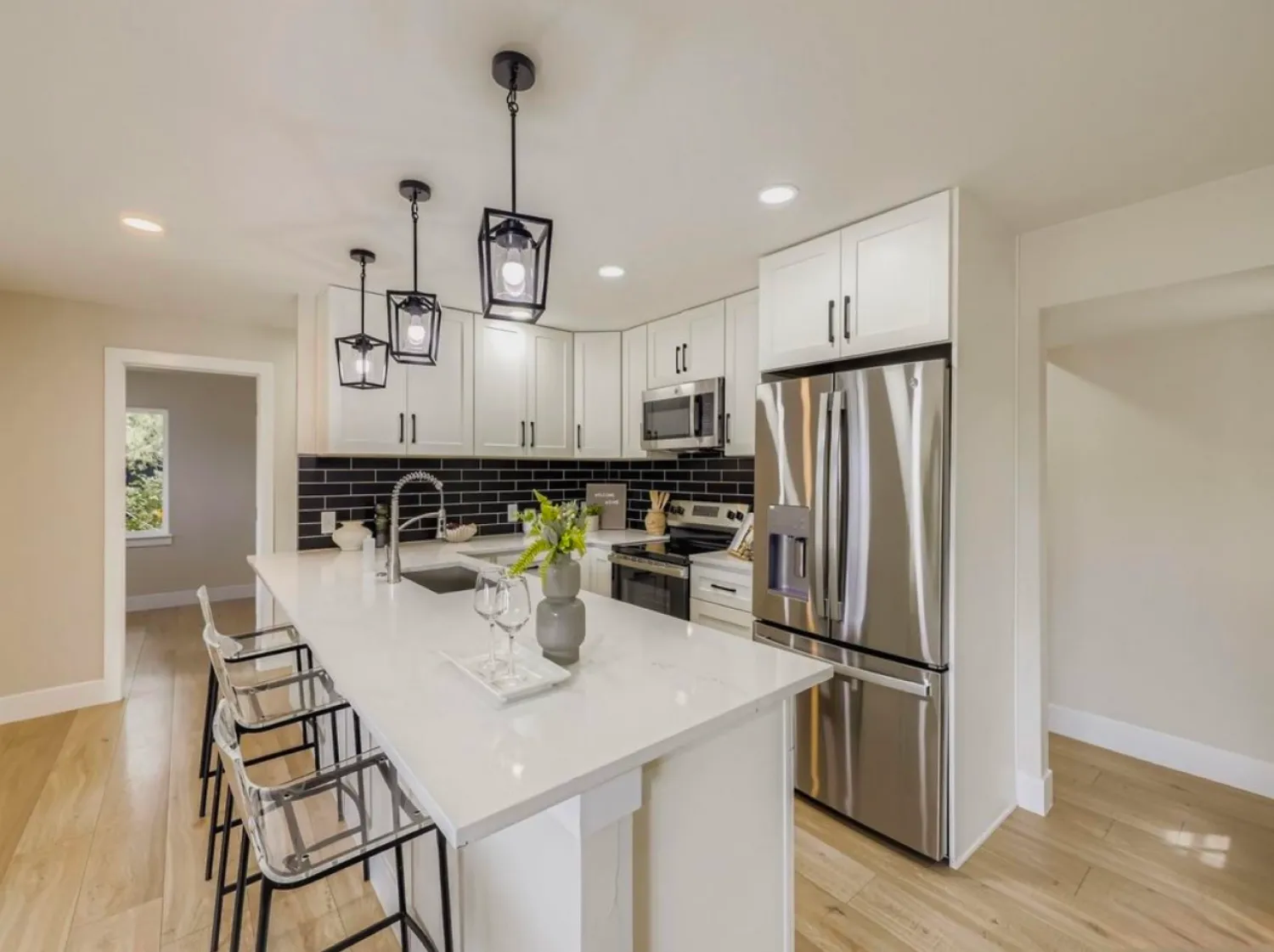 residential-interior-22 Modern kitchen with white cabinets, black tile backsplash, stainless appliances, and an island with clear stools.