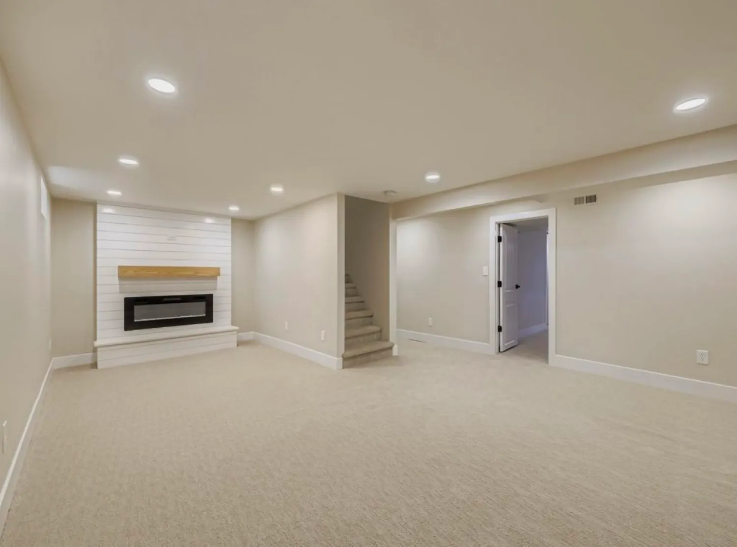 residential-interior-23 Spacious finished basement with beige carpet, recessed lights, fireplace, and stairs leading upstairs.
