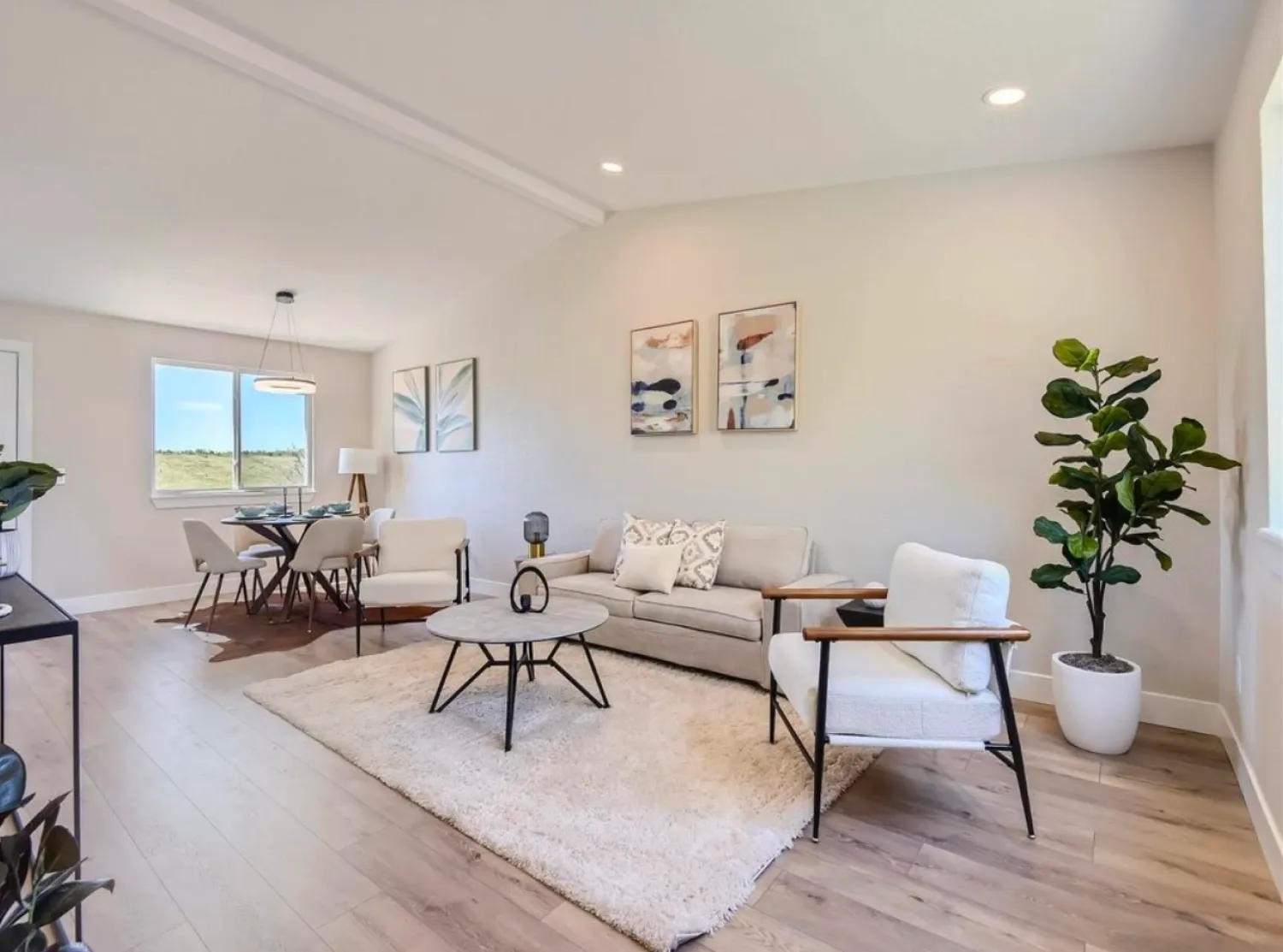 residential-interior-24 Modern living room with light furniture, a rug, potted plant, and dining area in the background.