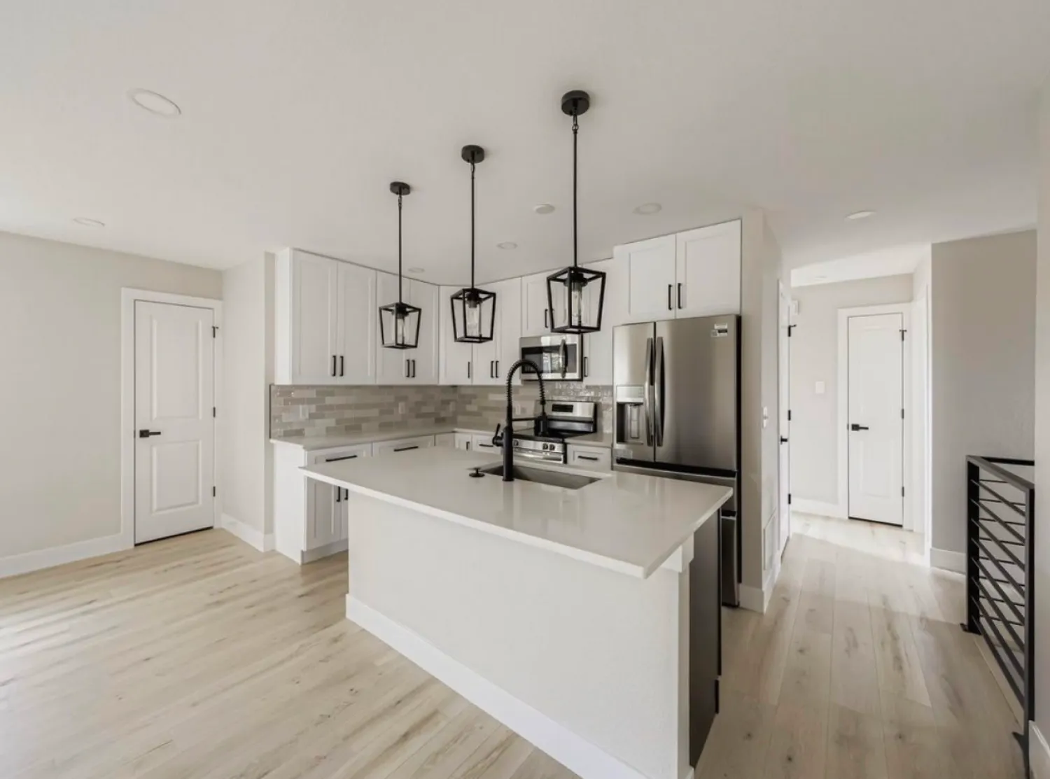residential-interior-25 Modern kitchen with white cabinets, stainless steel appliances, island, and three black pendant lights.