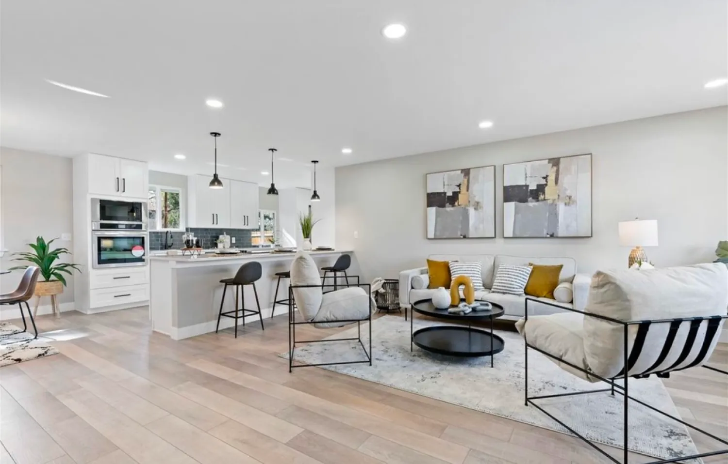 residential-interior-29 Modern open kitchen and living room with neutral tones, abstract art, and cozy seating with yellow accents.