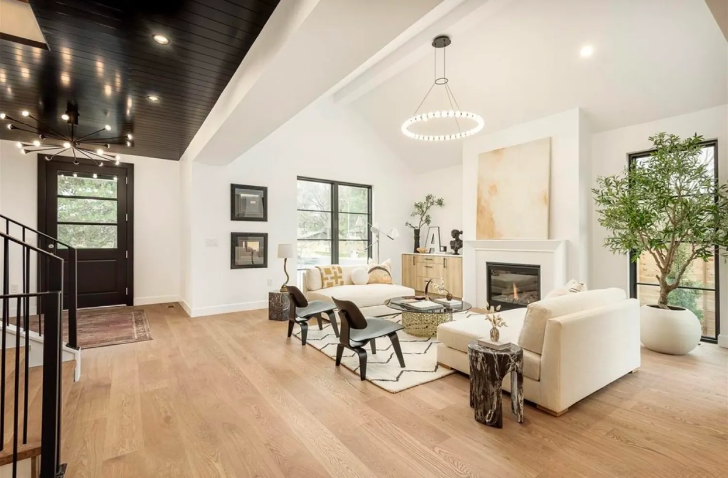 residential-interior-3 Modern living room with light wood floors, white walls, large windows, and stylish furniture around a fireplace.