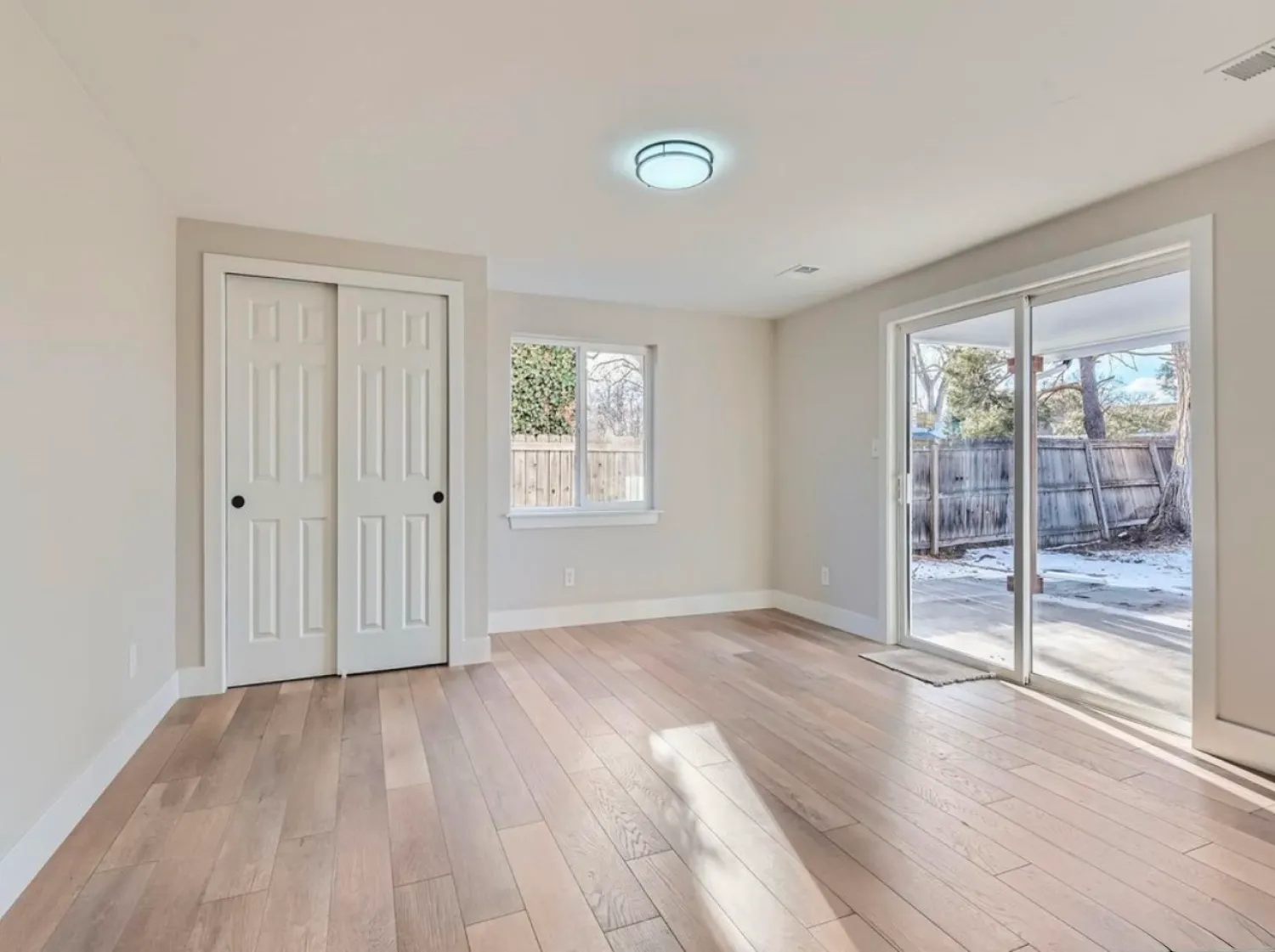 residential-interior-32 Bright empty room with wood floors, closet, window, and sliding glass door opening to a fenced backyard.