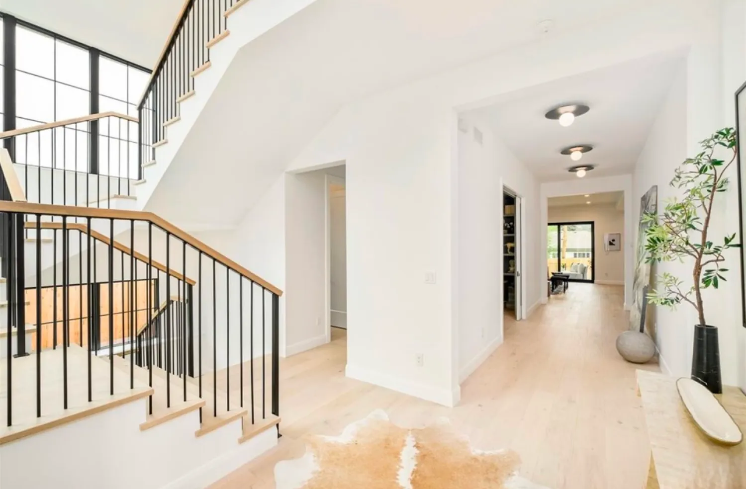 residential-interior-34 Bright hallway with light wood floors, modern staircase, and minimal decor, leading to a sunlit room.