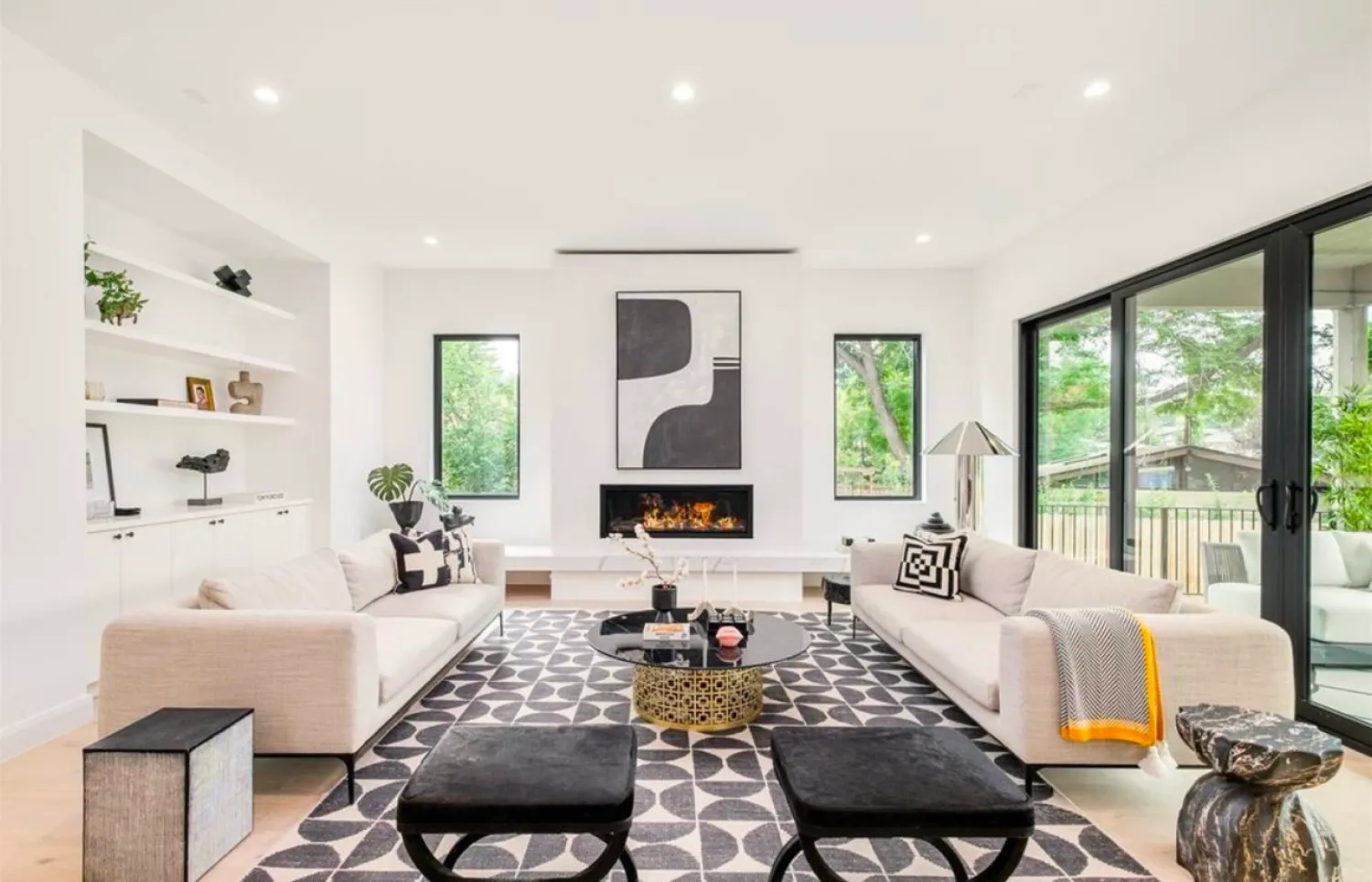 residential-interior-36 Modern living room with two white sofas, patterned rug, fireplace, abstract art, and large windows.