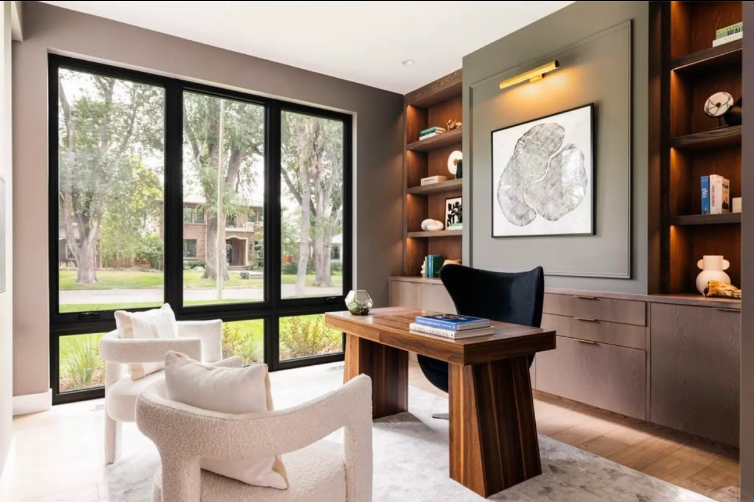 residential-interior-39 Modern home office with wood desk, chairs, built-in shelves, large windows, and abstract wall art.