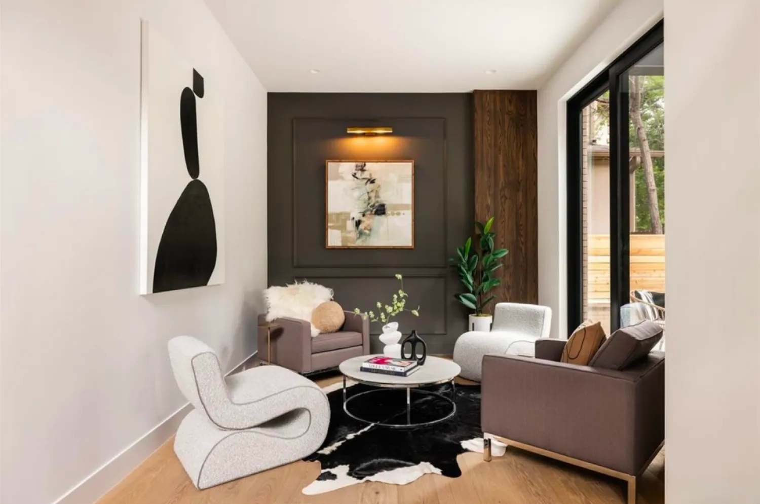residential-interior-40 Modern sitting area with cozy chairs, abstract art, a round coffee table, and a large window with outdoor view.