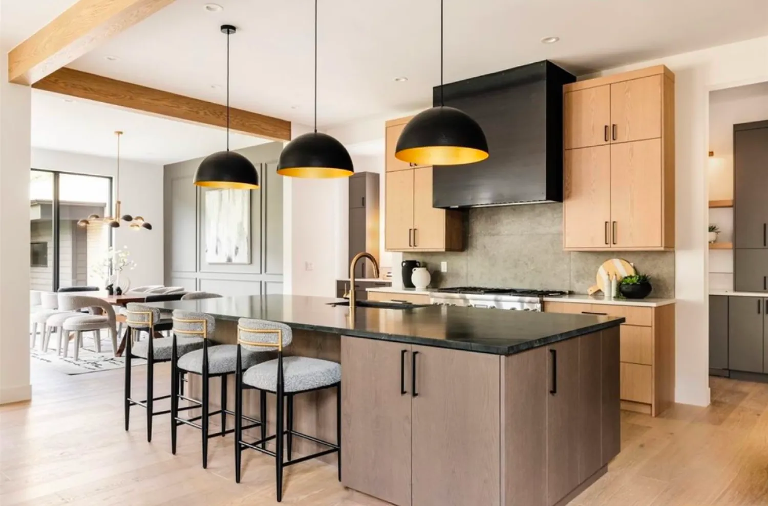residential-interior-41 Modern kitchen with black island, three pendant lights, wood cabinets, and stools with a dining area in back.