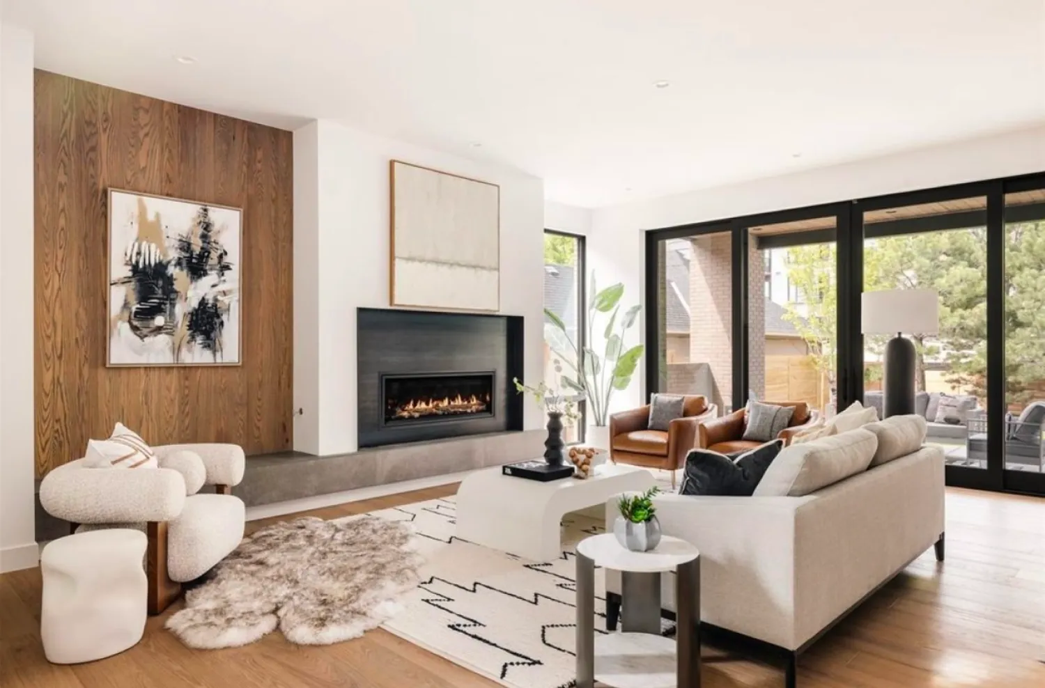 residential-interior-42 Modern living room with fireplace, neutral furniture, large windows, abstract art, and cozy rugs.