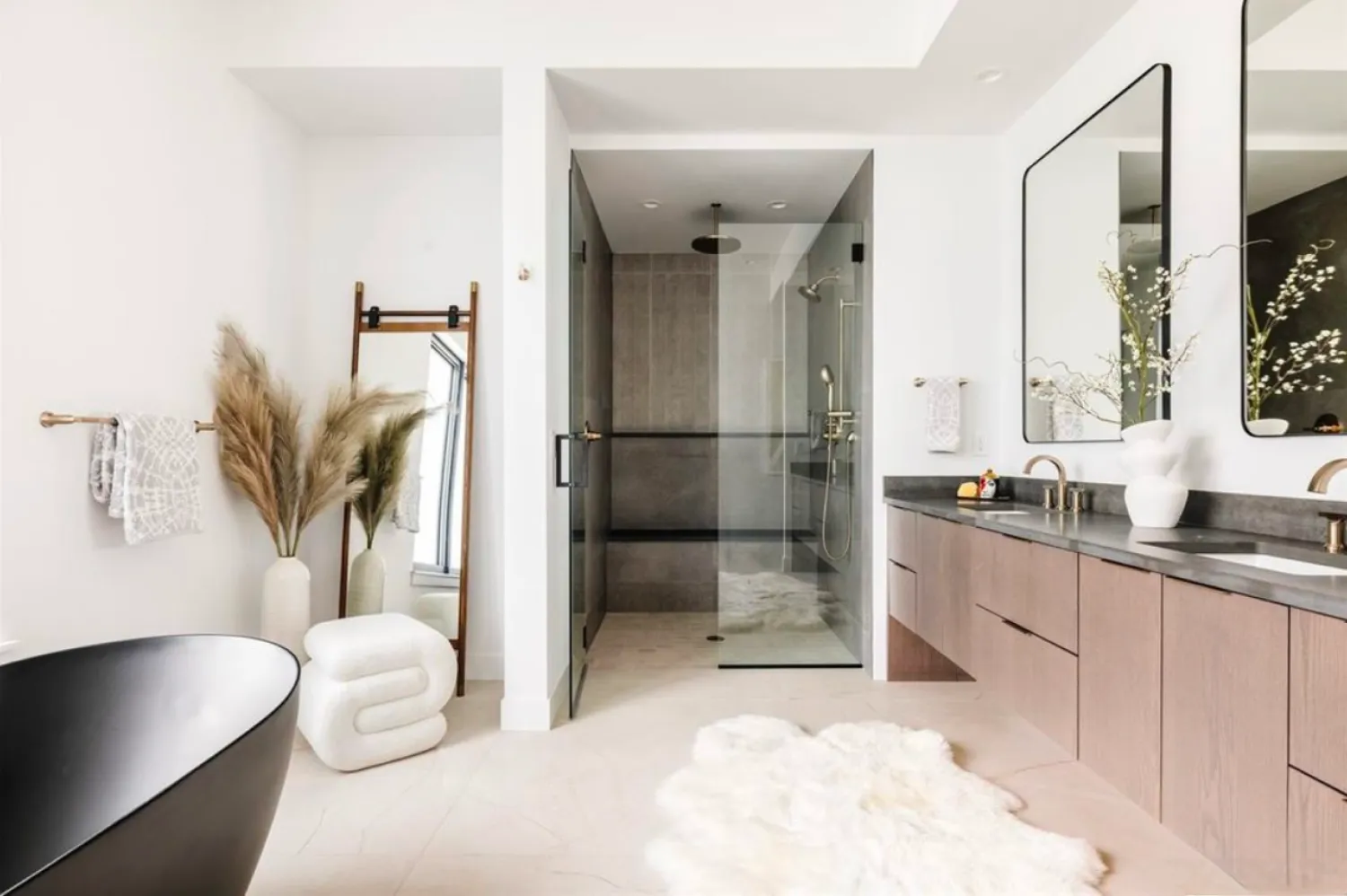 residential-interior-45 Modern bathroom with glass shower, double sinks, pampas grass, and a black bathtub.