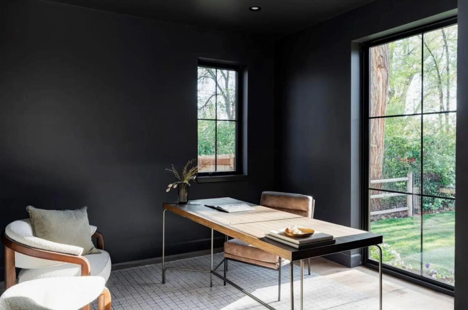 residential-interior-47 Minimalist office with black walls, modern furniture, large windows, and a view of a green backyard.