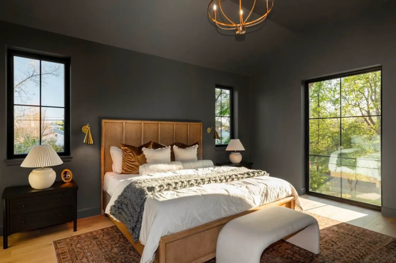 residential-interior-48 Modern bedroom with dark walls, large windows, a wooden bed, white bedding, and natural light streaming in.