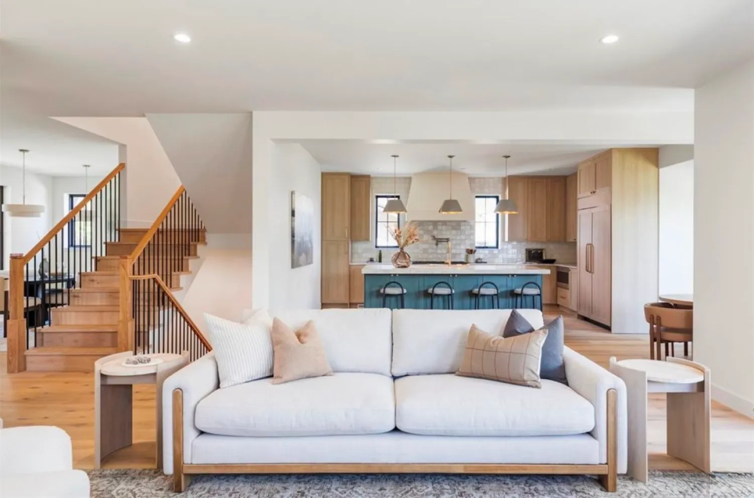 residential-interior-52 Modern living room with white sofa, wood accents, and view of stylish kitchen and staircase in open floor plan.