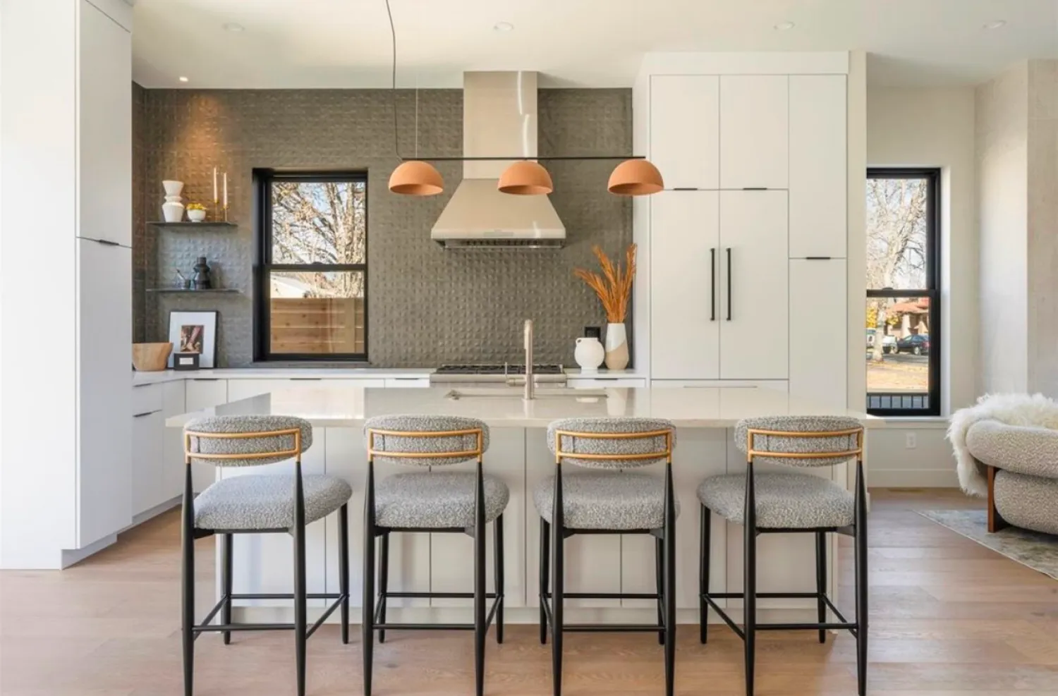 residential-interior-54 Modern kitchen with white cabinets, gray tiled backsplash, island, four stools, and pendant lights.