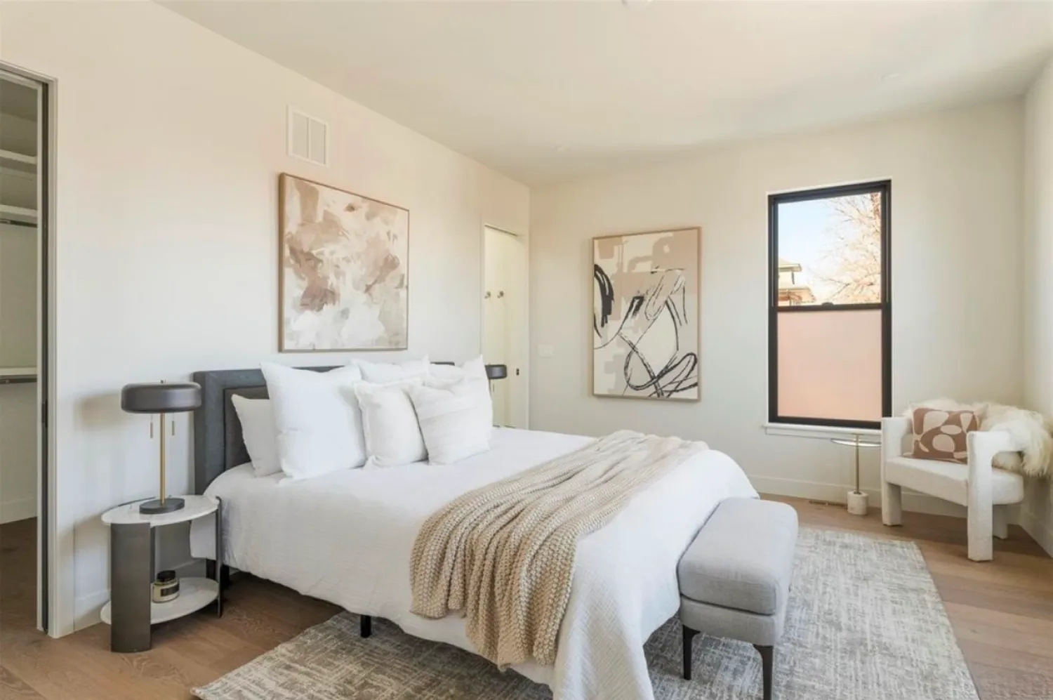 residential-interior-57 Minimalist bedroom with a bed, neutral decor, abstract art, a chair, and natural light from one window.