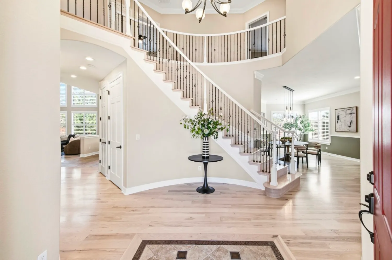 residential-interior-58 Bright entryway with a curved staircase, light wood floors, and a black table with a vase of flowers.