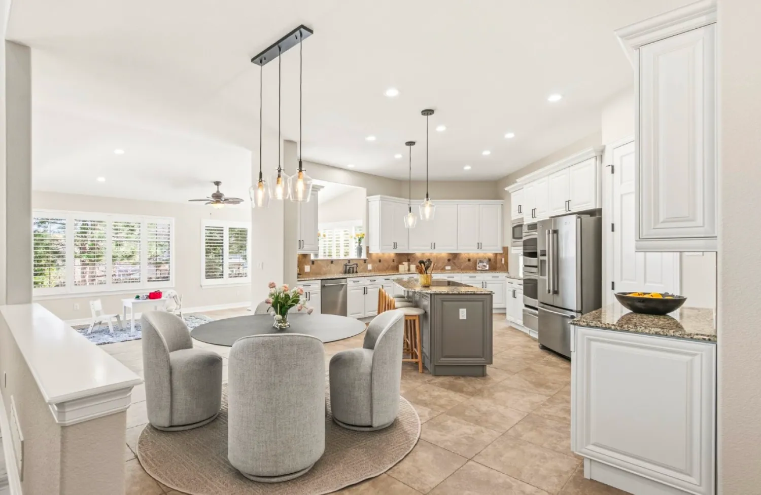 residential-interior-62 Modern kitchen with white cabinets, round dining table, gray chairs, pendant lights, and neutral decor.
