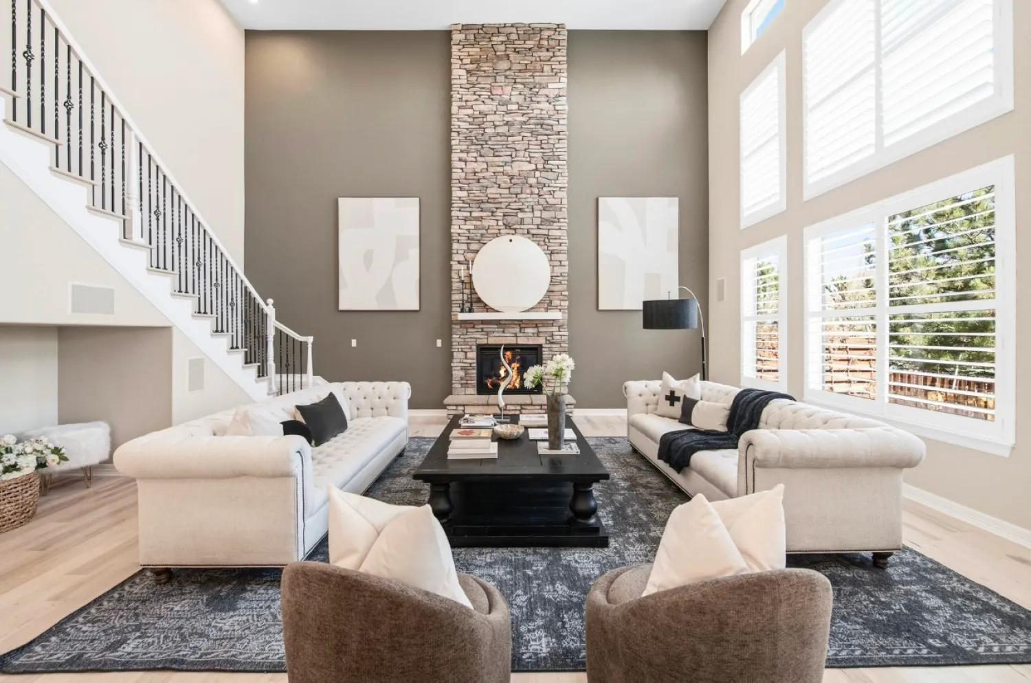 residential-interior-63 Modern living room with high ceilings, stone fireplace, two white sofas, two chairs, and large windows.
