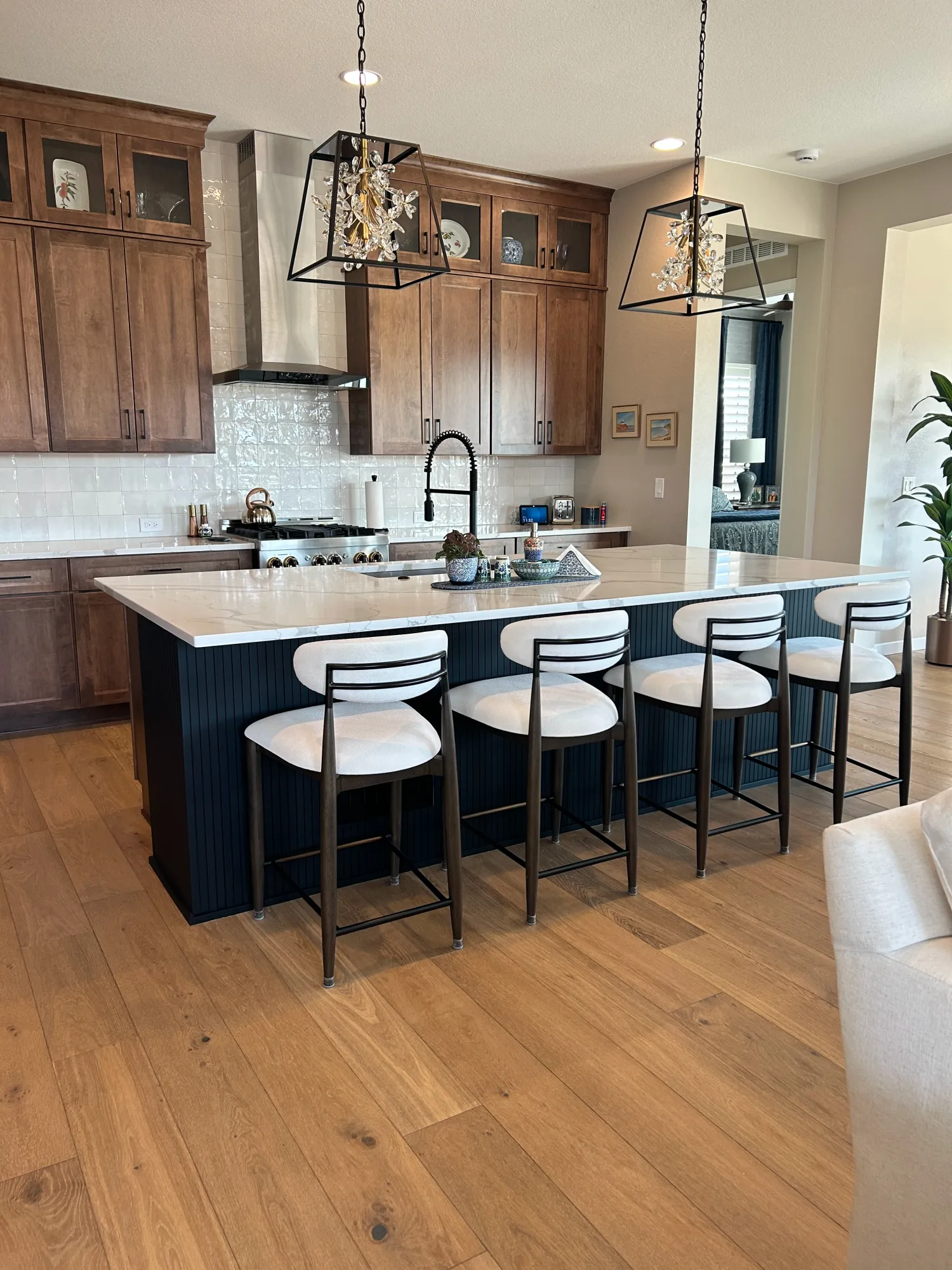 Modern kitchen with a large island, four barstools, wood cabinets, pendant lights, and hardwood floors.