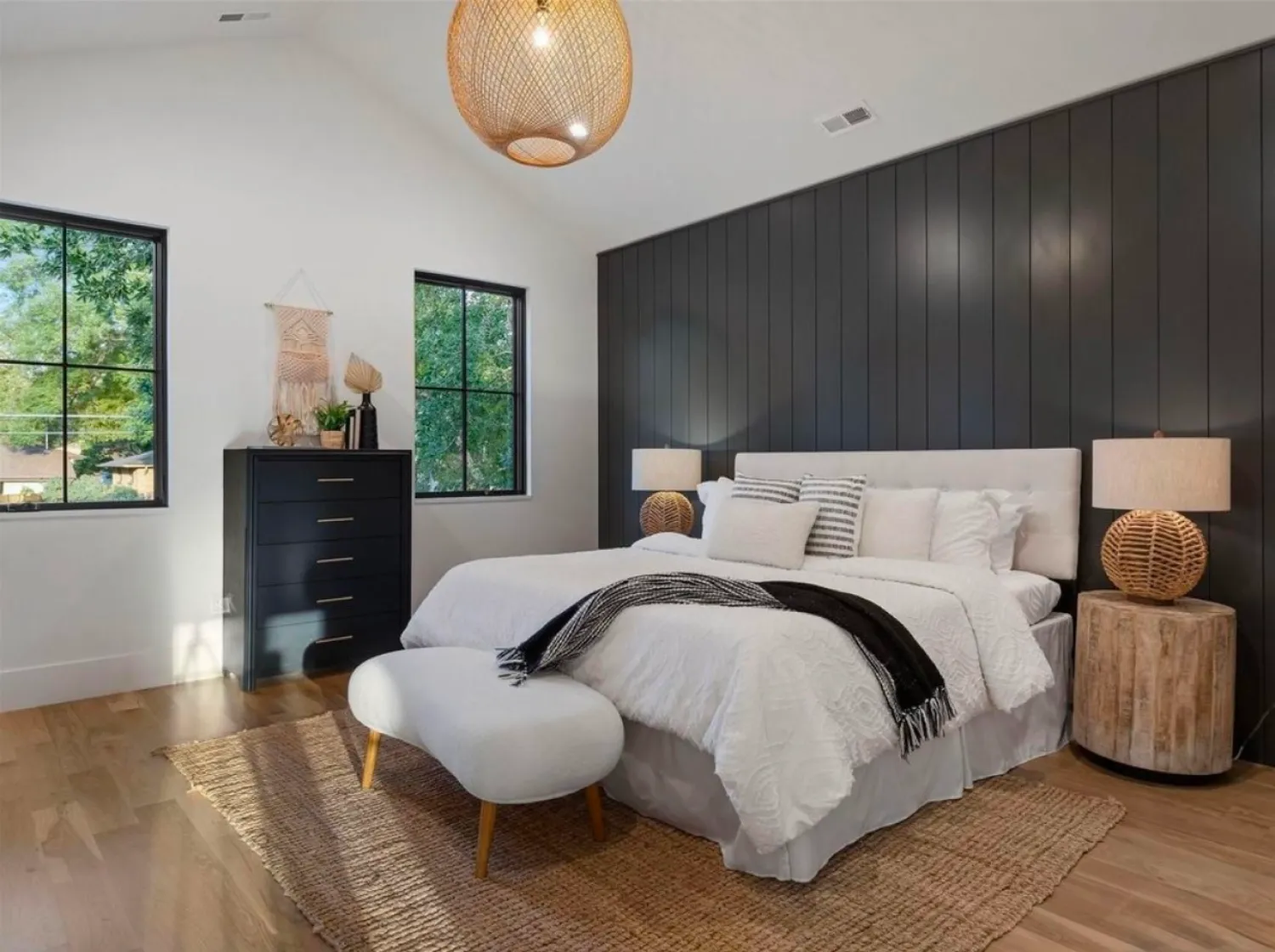 residential-interior-8 Modern bedroom with black accent wall, white bedding, two lamps, chest of drawers, and woven decor.