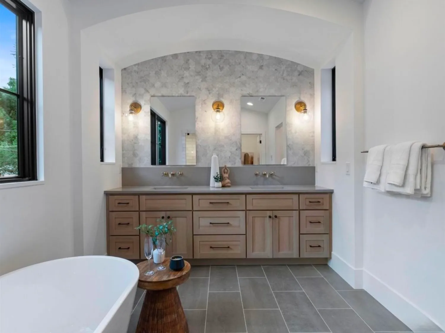 residential-interior-9 Modern bathroom with double sink vanity, round mirrors, gold sconces, tub, and wood accents.